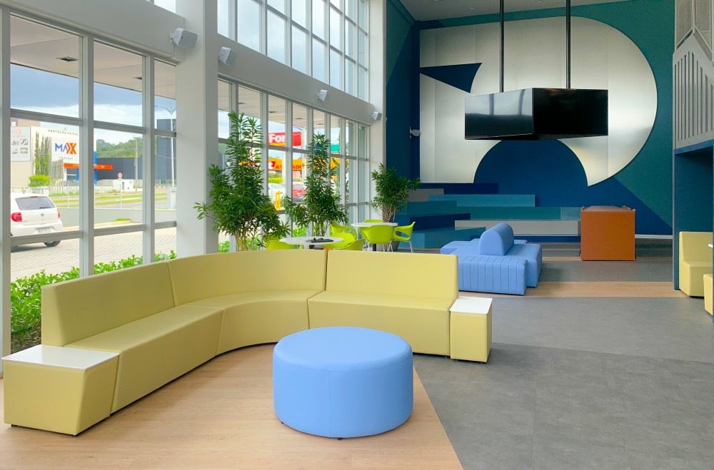 Lounge iluminado com sofás modulares amarelos e pufe azul