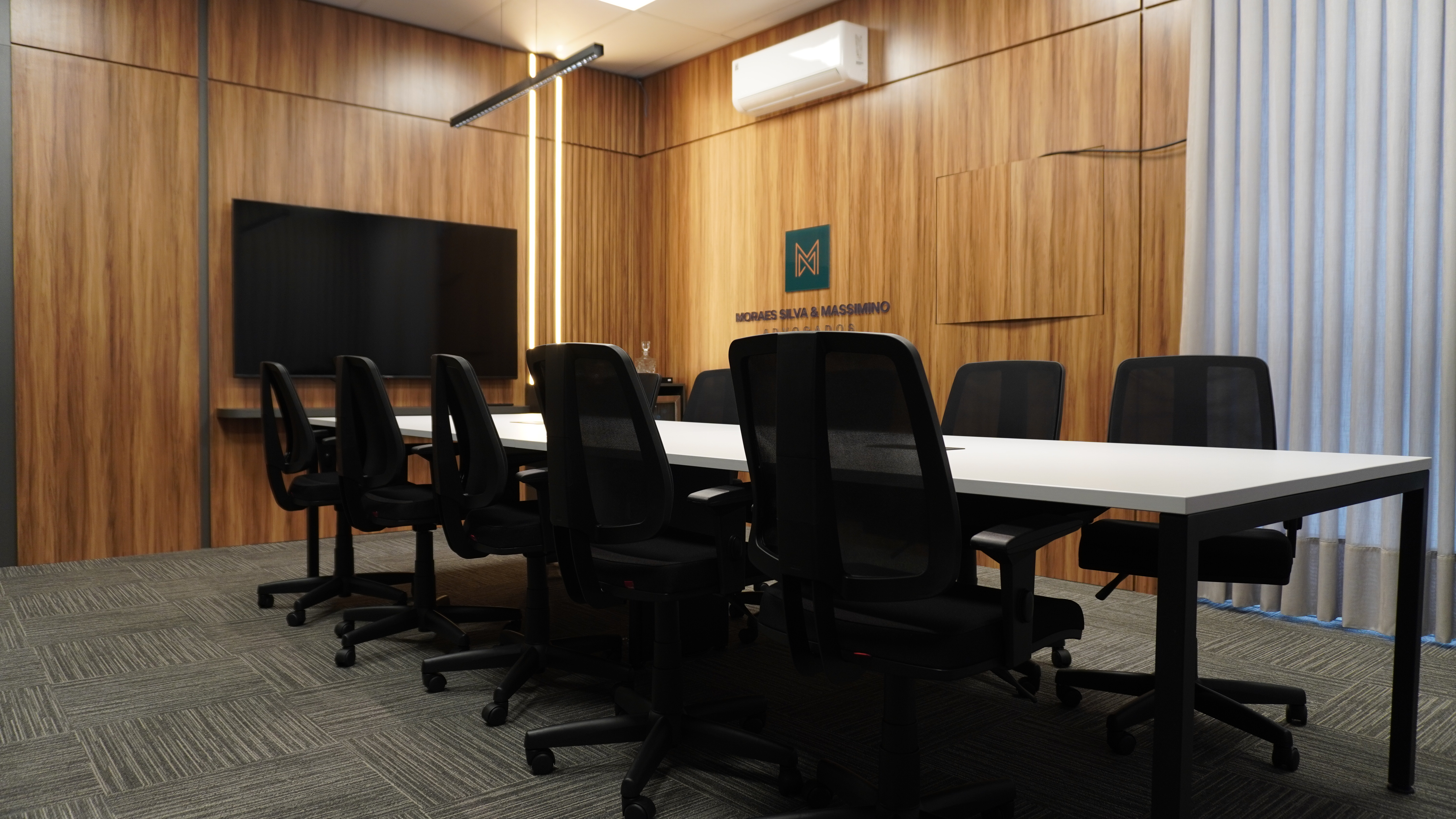 Ambiente corporativo com mesa branca, cadeiras pretas e paredes com acabamento amadeirado